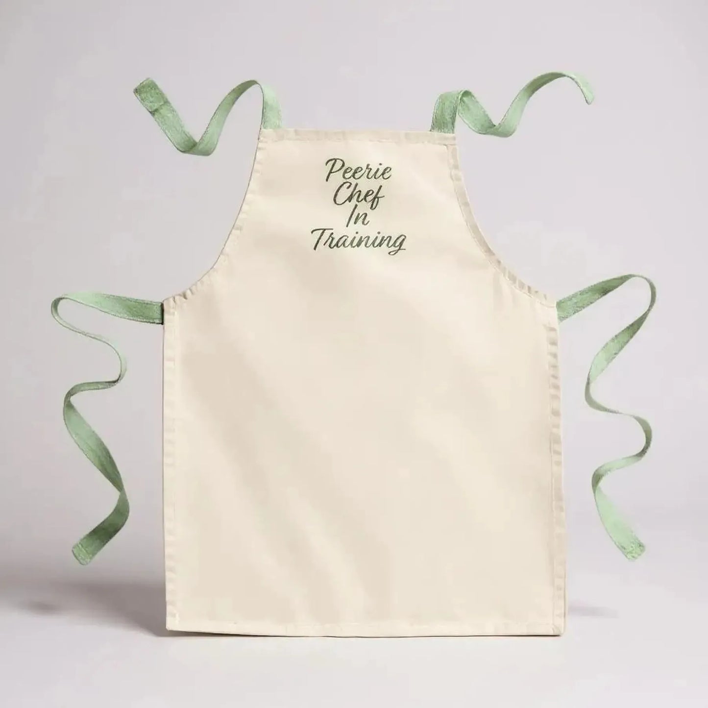 Cream cotton apron with green trim and "Peerie Chef In Training" embroidery.