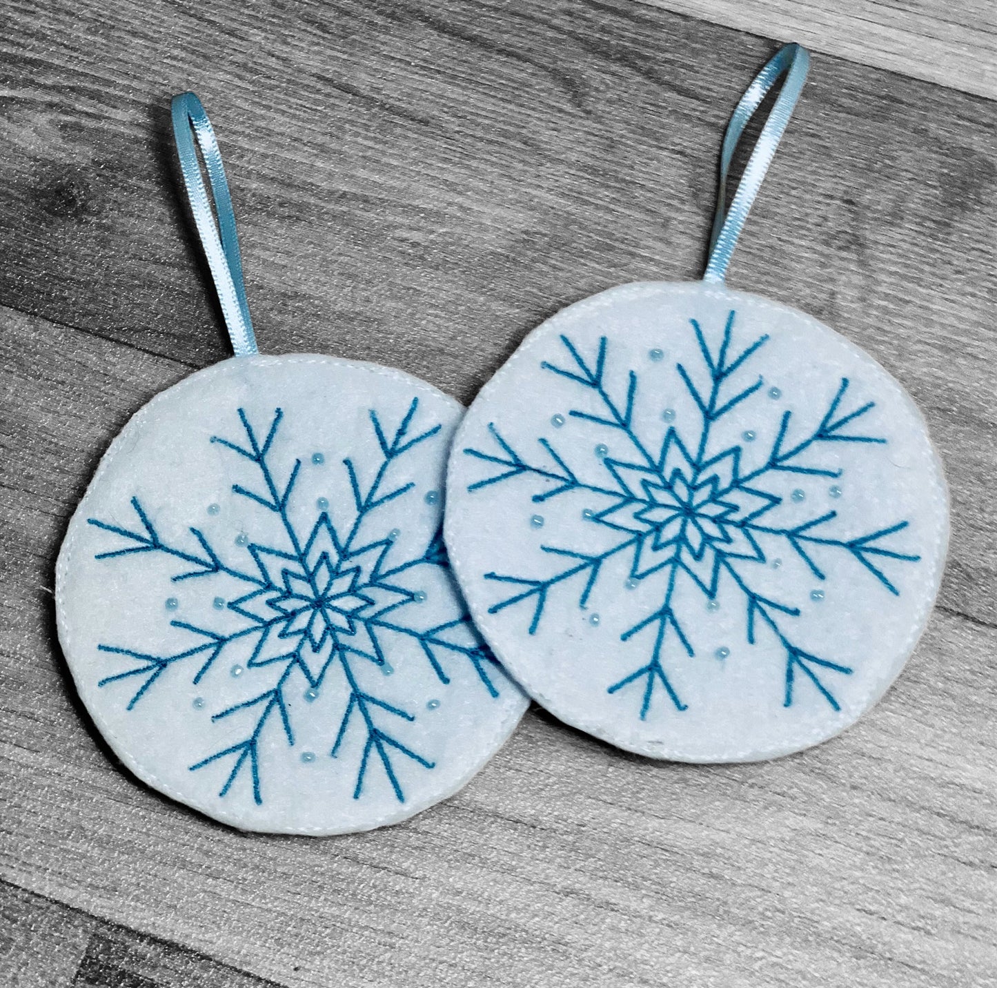 Embroidered white felt snowflake Christmas tree decorations with blue stitching and beads.