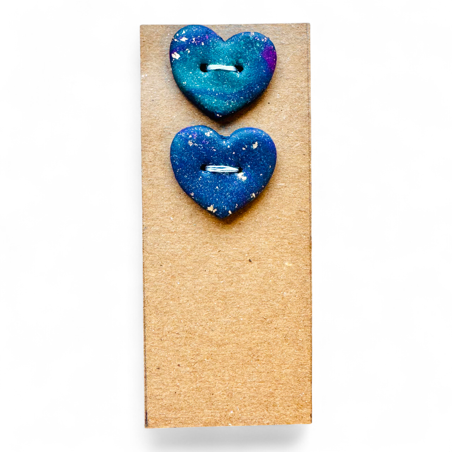 Two handmade heart-shaped buttons with a blue and purple galaxy design and gold flecks.
