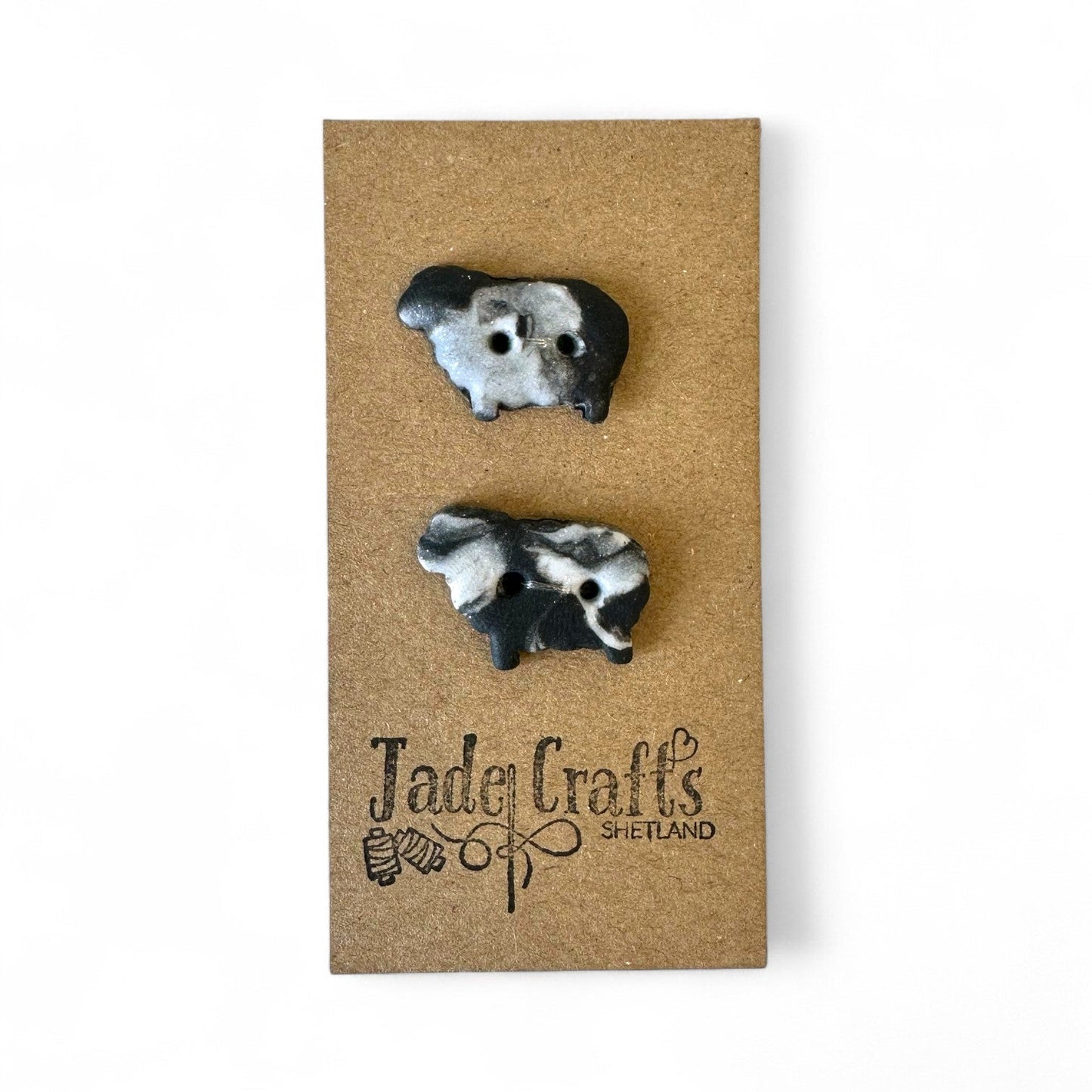 Two handmade black and white sheep buttons on a brown card with a logo.