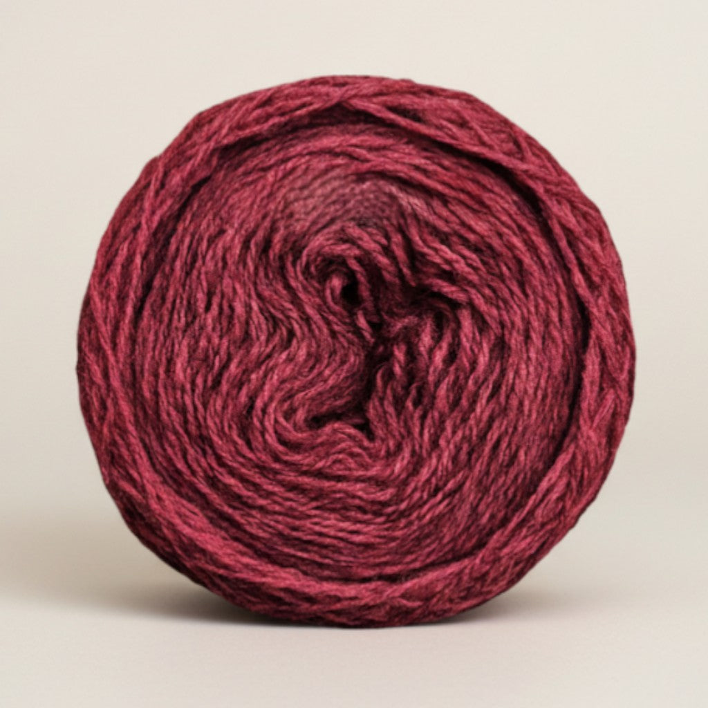 A round cake of Uradale 100% Shetland wool yarn in a deep burgundy Selfheal colourway.