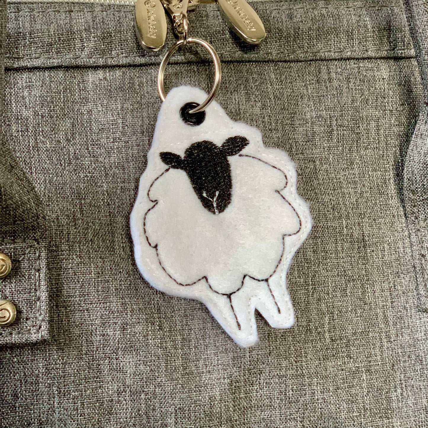 Shetland sheep keyring made of white felt with black face and brown stitching.