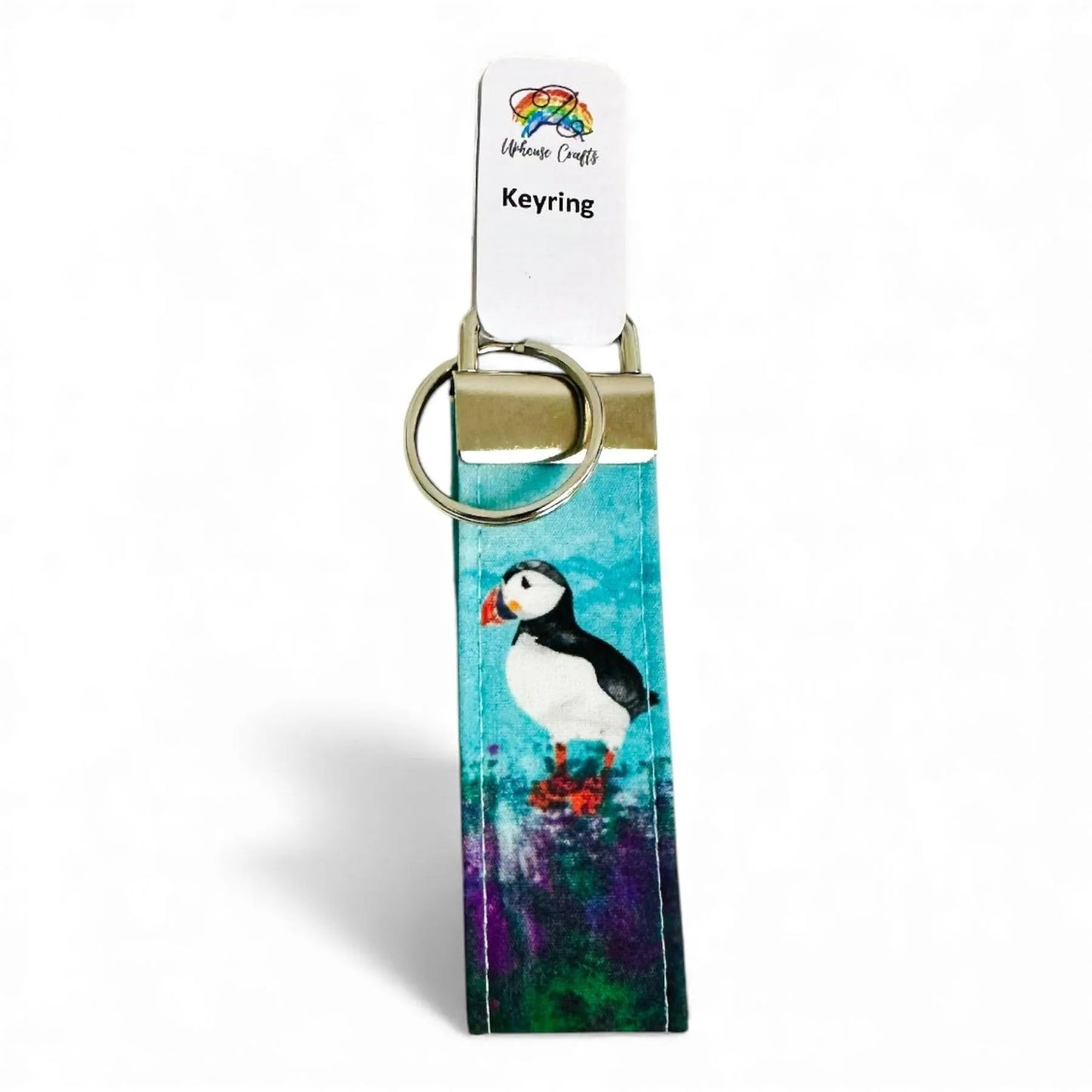 Fabric keyring featuring a puffin illustration on a blue and purple background with a metal clasp.