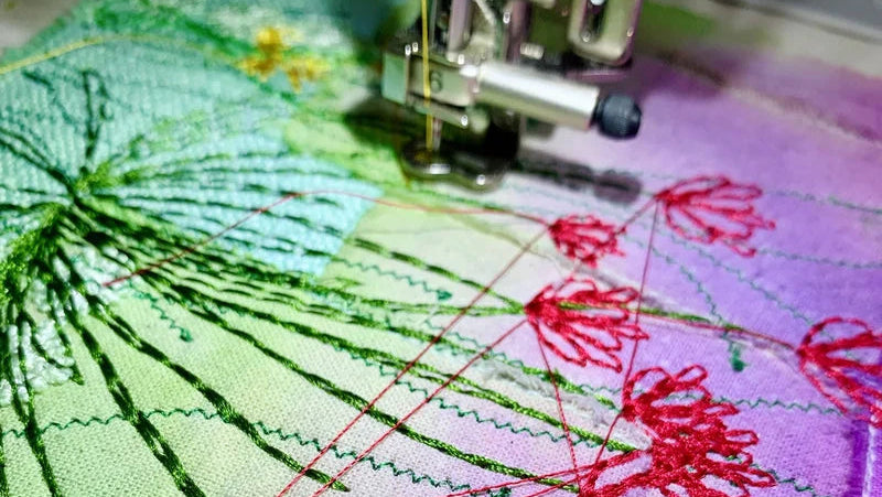 Embroidery machine stitching red floral patterns on fabric with green and purple backgrounds.