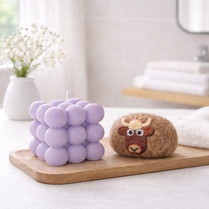 Handmade purple bubble candle and a brown felted soap with a cow face on a wooden tray.