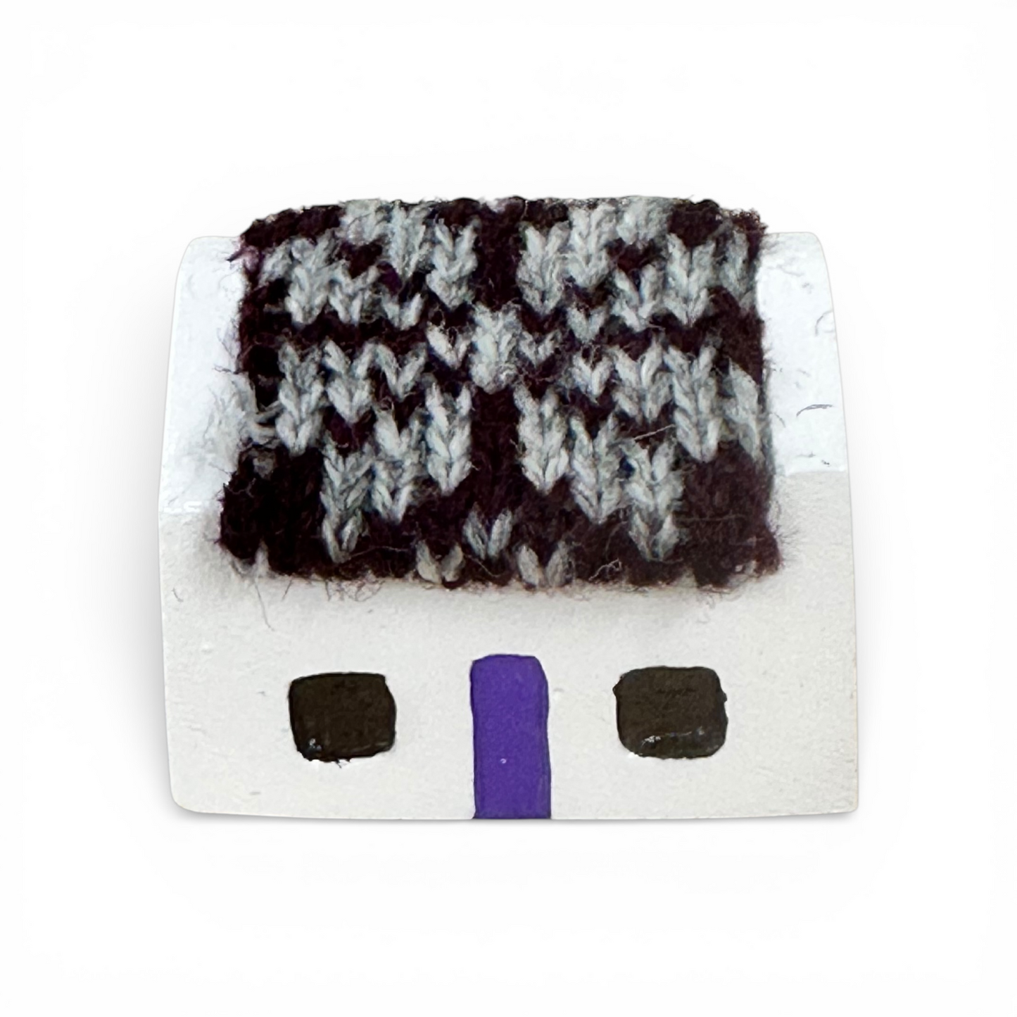 Handmade white croft house with a purple door and a grey and black knitted wool roof.