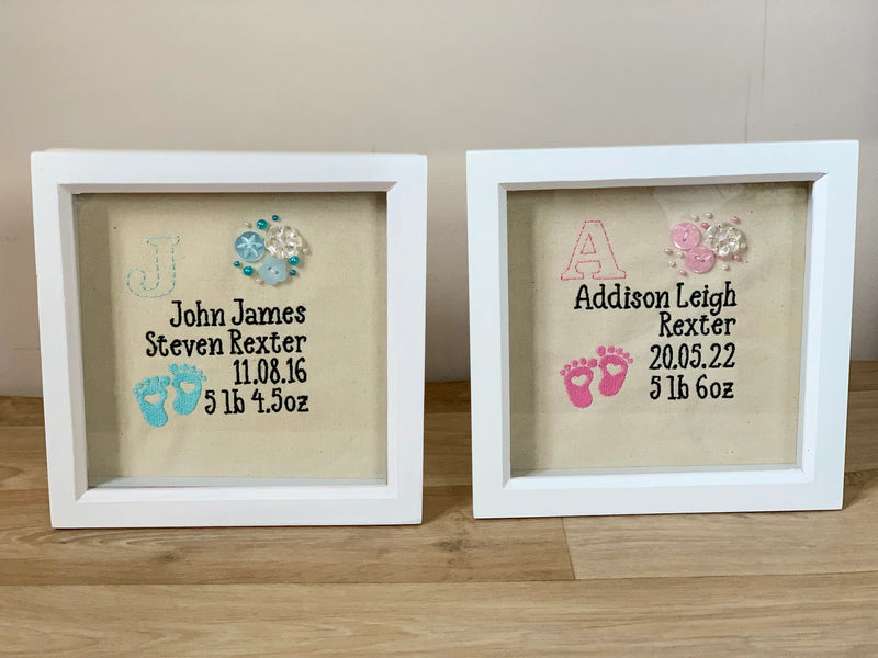 Two framed baby announcements with names and birth details on a wooden surface.
