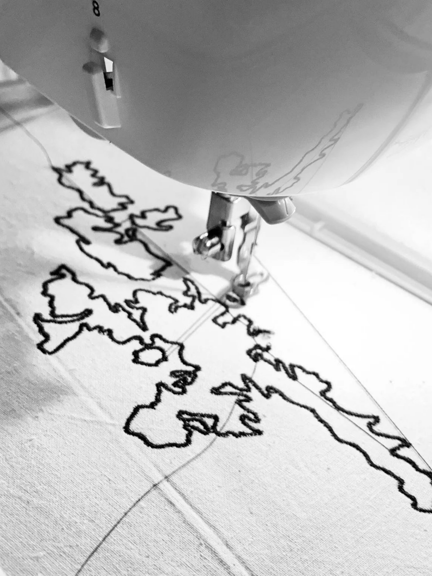 Person using a embroidery machine on a white cotton with a black Shatland Isle oitline.