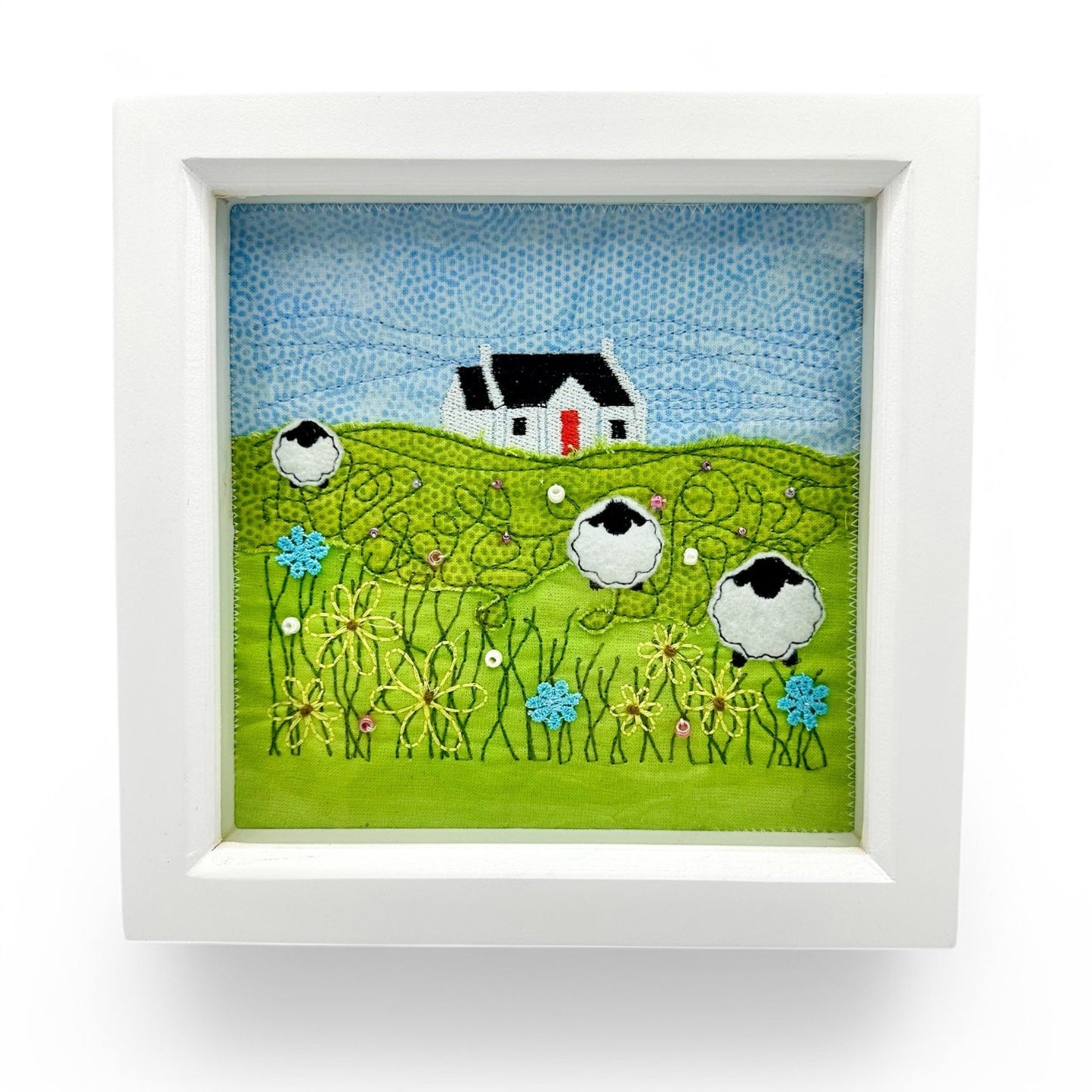 Embroidered art of a croft house on a hill with sheep and flowers.