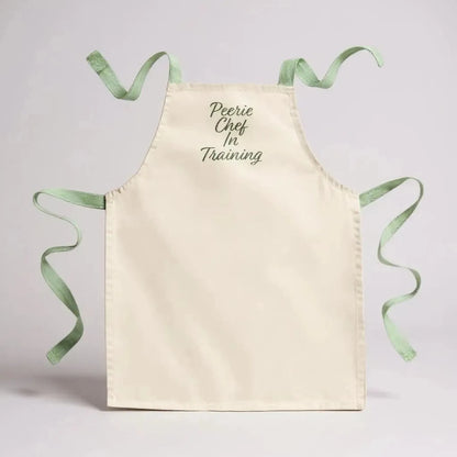 Cream cotton apron with green trim and "Peerie Chef In Training" embroidery.