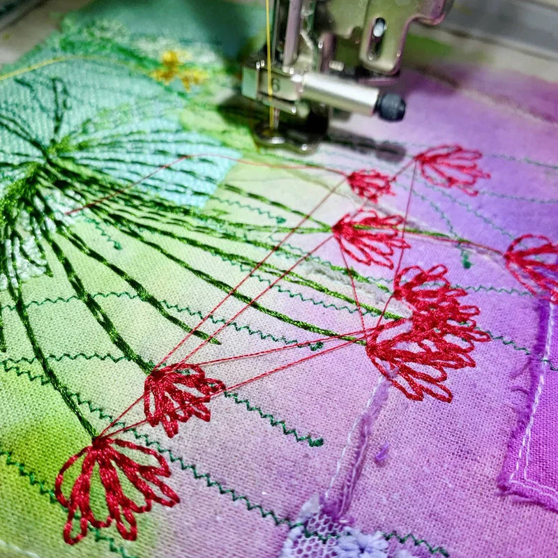 Embroidery machine stitching red floral patterns on fabric with green and purple backgrounds.