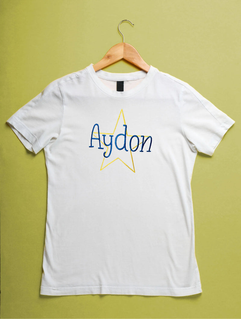 White t-shirt with 'Aydon' design on a wooden hanger against a green background