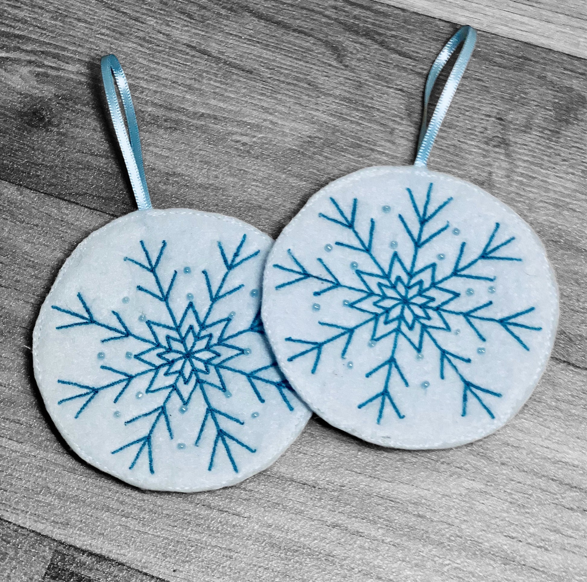 Embroidered white felt snowflake Christmas tree decorations with blue stitching and beads.