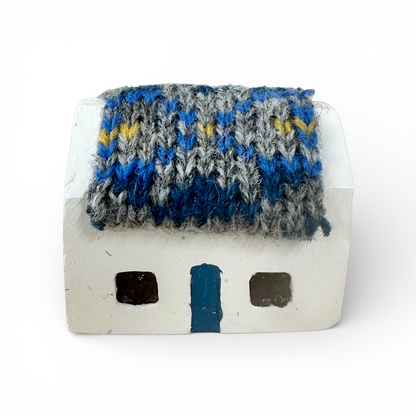 Handmade white croft house with a blue and grey knitted wool roof and a blue door.