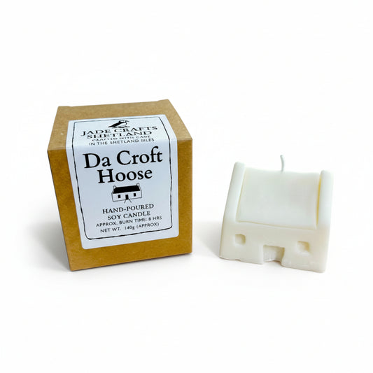 A white, house-shaped soy candle next to its brown cardboard packaging.