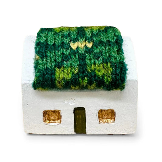 Handmade miniature white croft house with a green knitted wool roof and gold-painted windows.