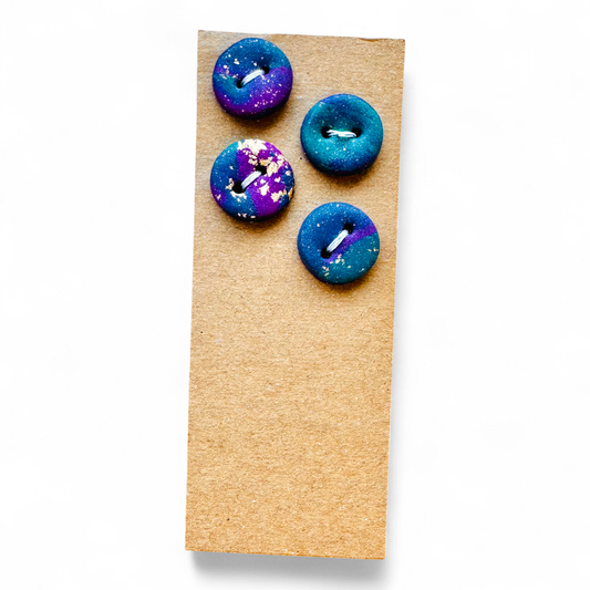Four handmade polymer clay buttons with a blue, purple, and teal marbled design and gold flecks.