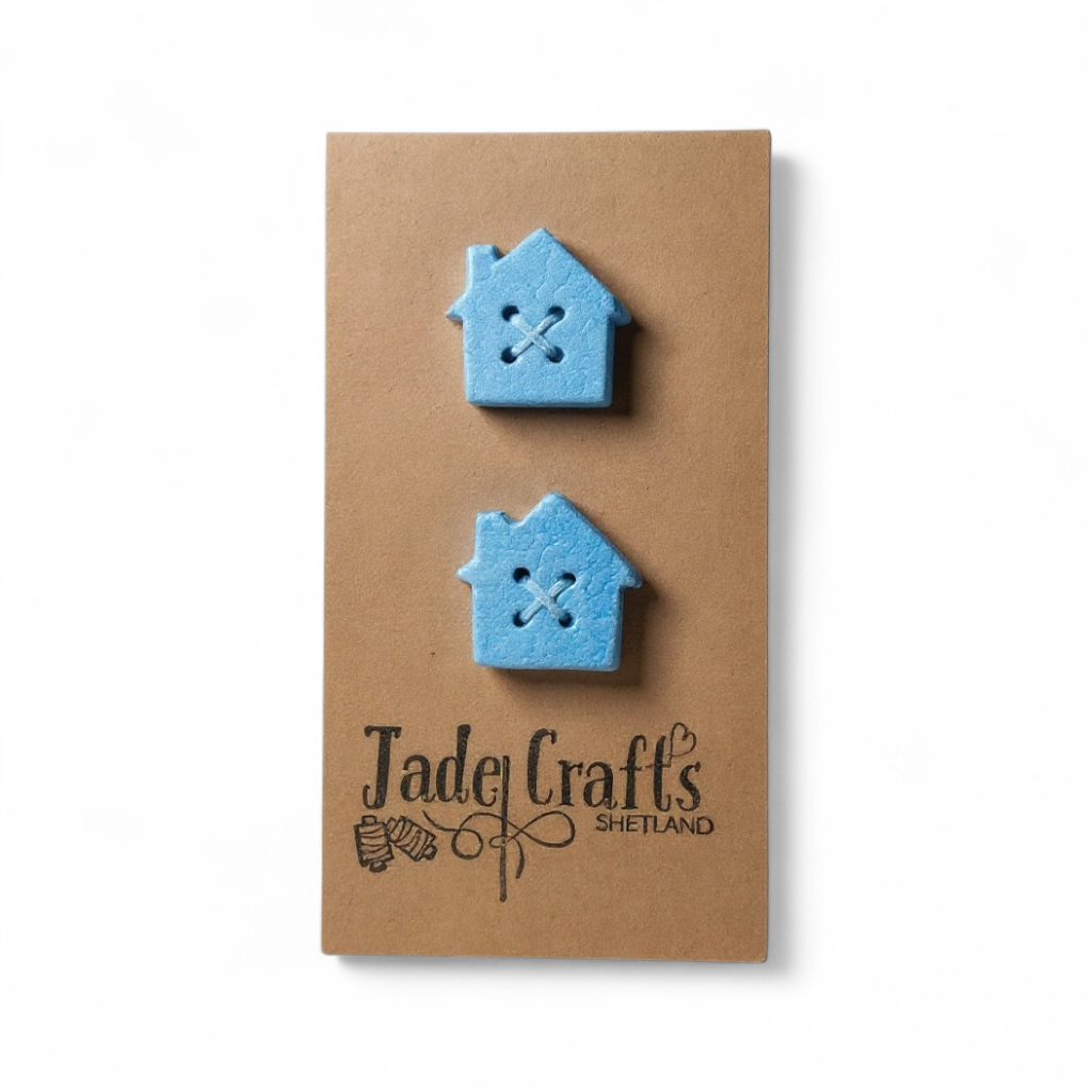 Two blue lace effect clay buttons shaped like croft houses on a brown card.