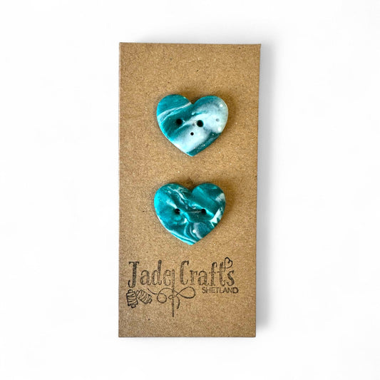 Two handmade teal and white marbled heart buttons on a brown card.