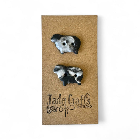 Two handmade black and white sheep buttons on a brown card with a logo.