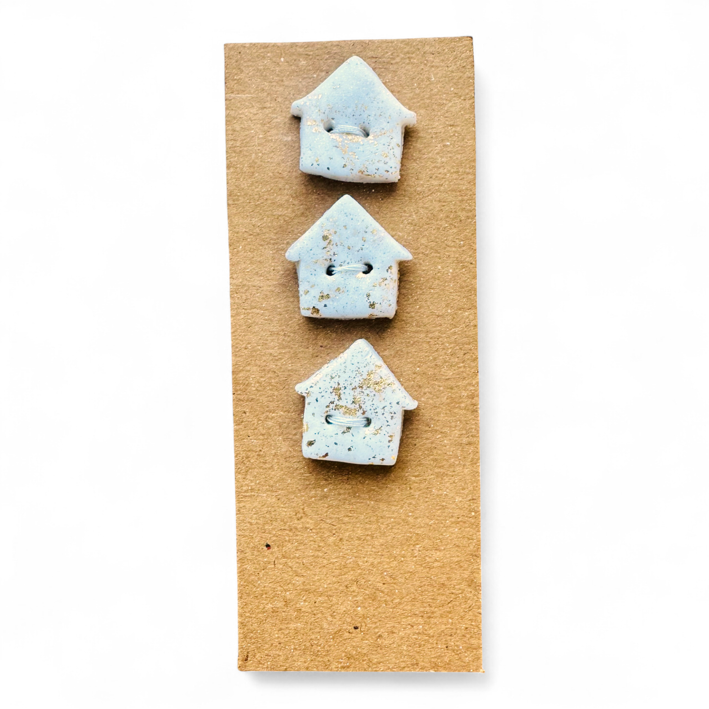 Three handmade light blue house-shaped buttons with gold flecks on a brown card.