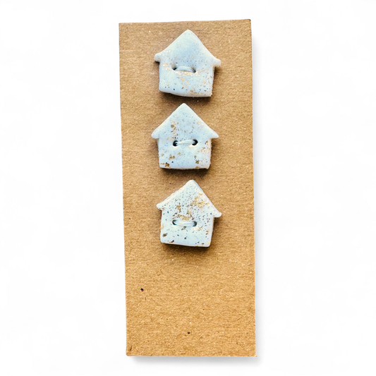 Three handmade light blue house-shaped buttons with gold flecks on a brown card.