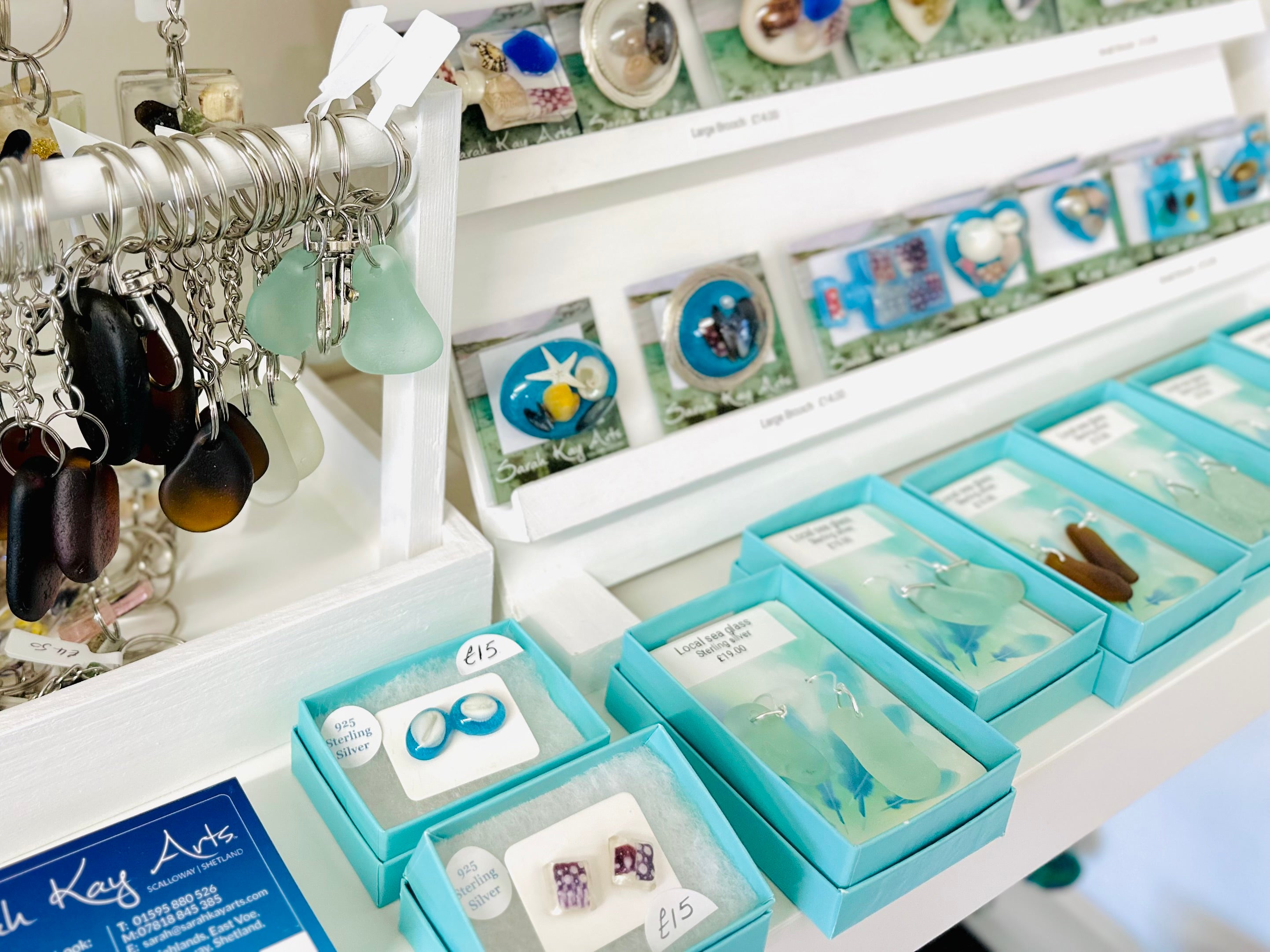 Display of earrings in turquoise boxes on a shelf with keychains above.