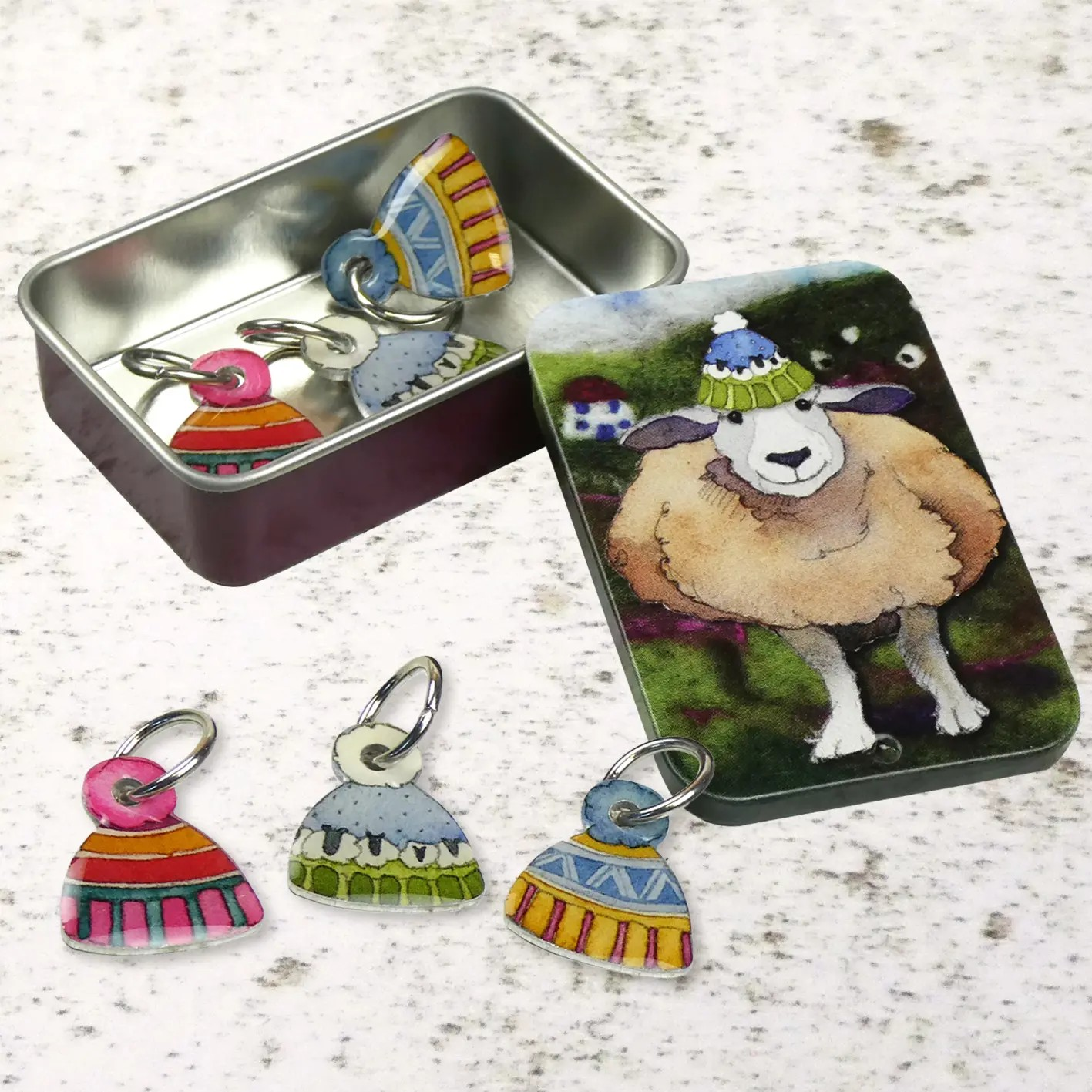 Six sheep hat stitch markers in a tin, with three outside and three inside.