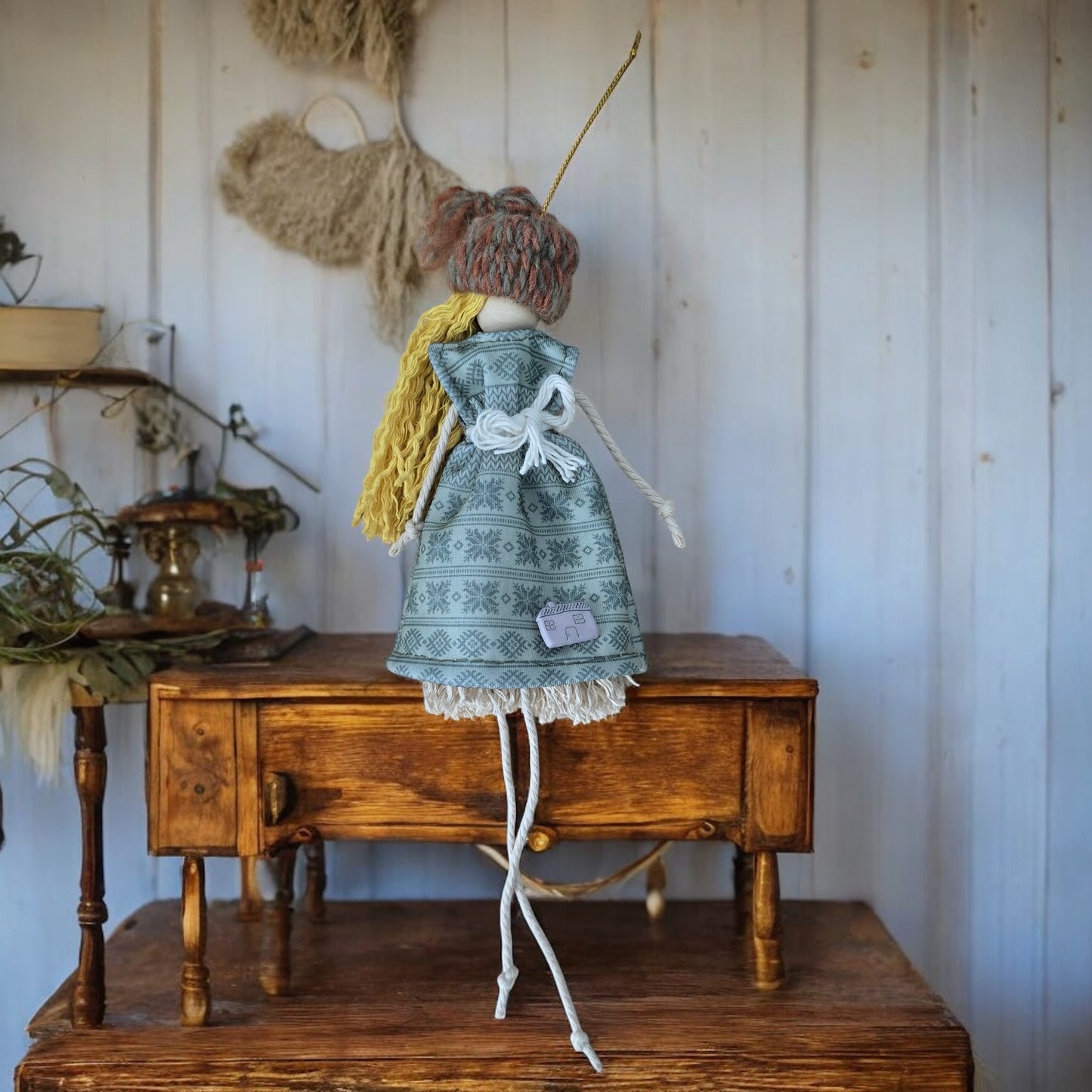 Handmade macramé doll with yellow hair, blue snowflake dress, and a small house charm.