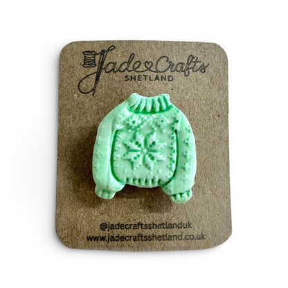 Hand-painted green clay brooch in the shape of a Fair Isle jumper on a brown card backing.