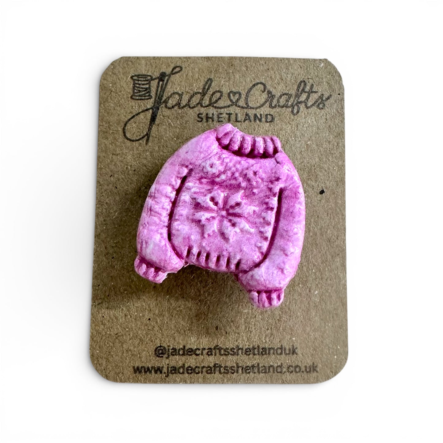 Hand-painted pink clay brooch in the shape of a Fair Isle jumper on a brown card backing.