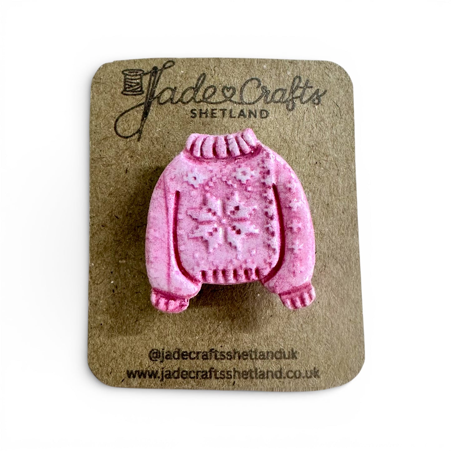 Hand-painted pink clay brooch in the shape of a Fair Isle jumper on a brown card backing.