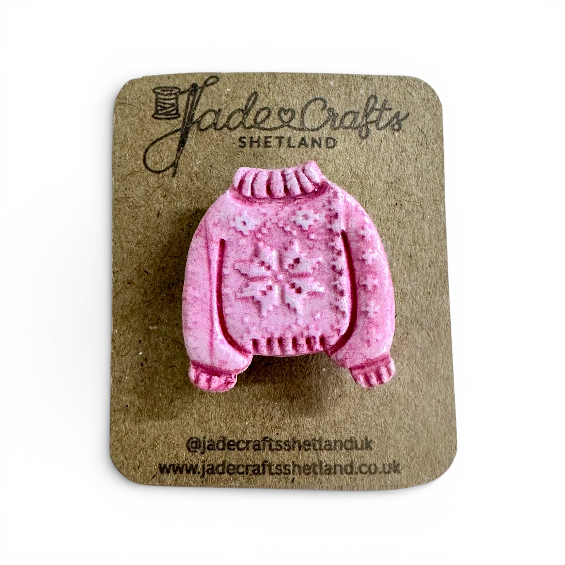 Hand-painted pink clay brooch in the shape of a Fair Isle jumper on a brown card backing.