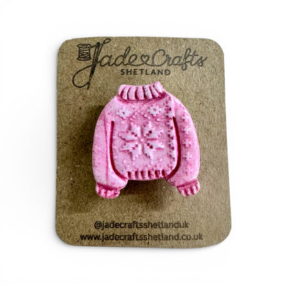 Hand-painted pink clay brooch in the shape of a Fair Isle jumper on a brown card backing.