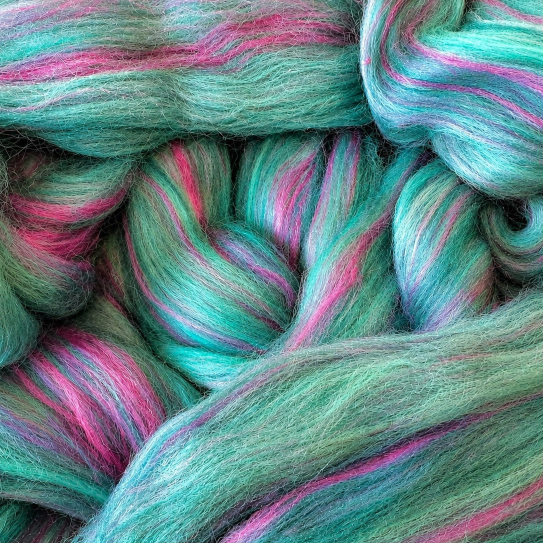 Close-up of fluffy fiber yarn in a variegated pattern of mint green, teal, and bright pink.