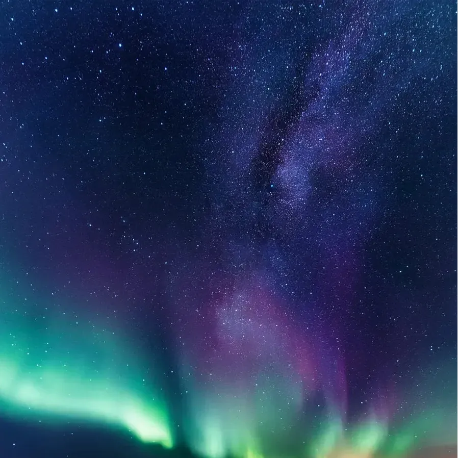 Aurora borealis over a mountainous landscape with stars in the sky.