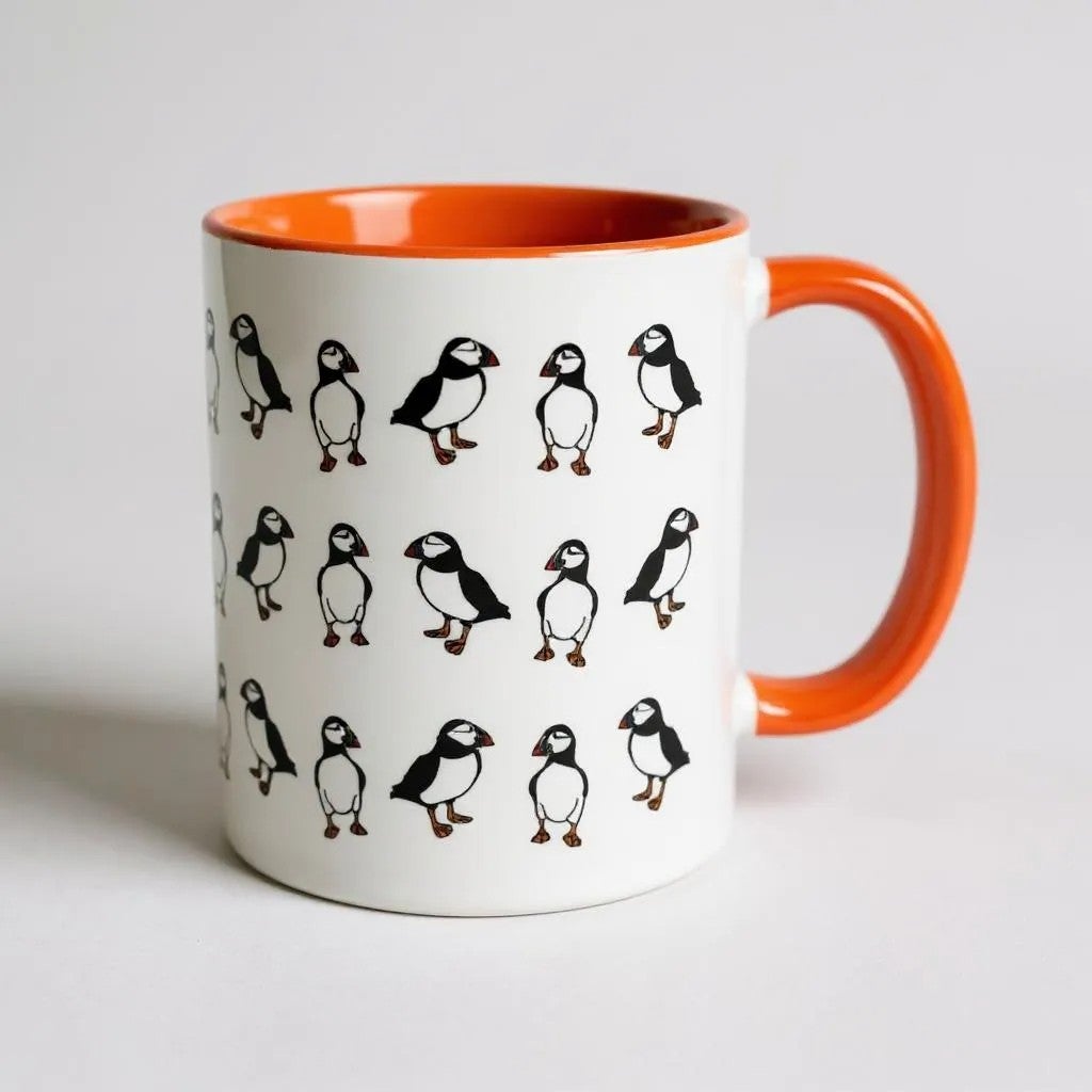 White ceramic mug with an orange handle and a pattern of puffins.
