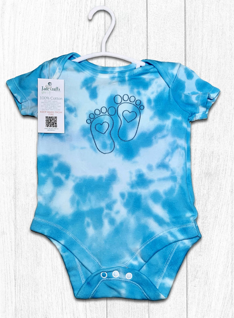 Blue tie-dye baby onesie with footprints on a white wooden background