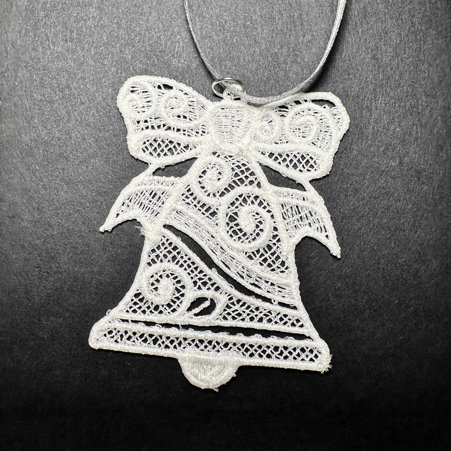White lace bell ornament with a bow on a dark background.