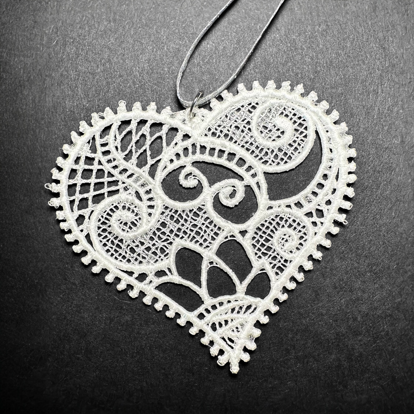White lace heart ornament with intricate scrollwork and scalloped edge.