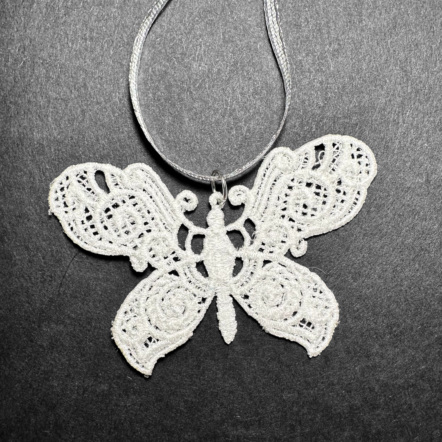 White lace butterfly ornament with silver ribbon on a dark background.