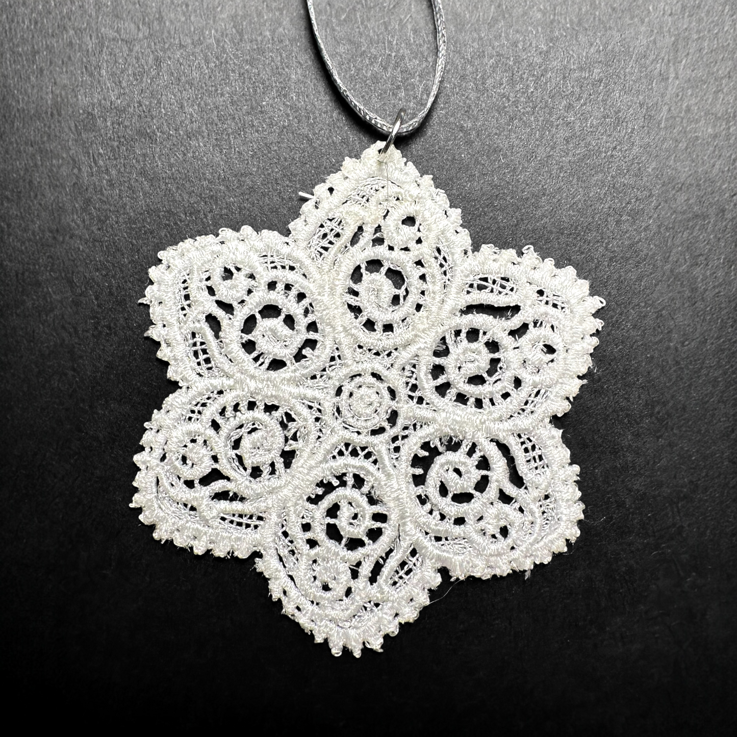 White lace snowflake Christmas tree ornament on a black background.