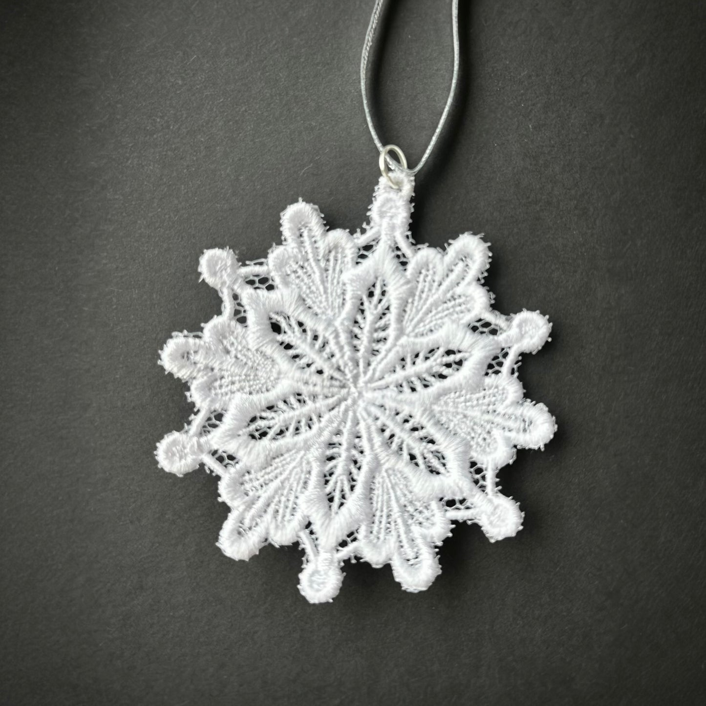 White lace snowflake Christmas tree ornament with a silver loop and string.