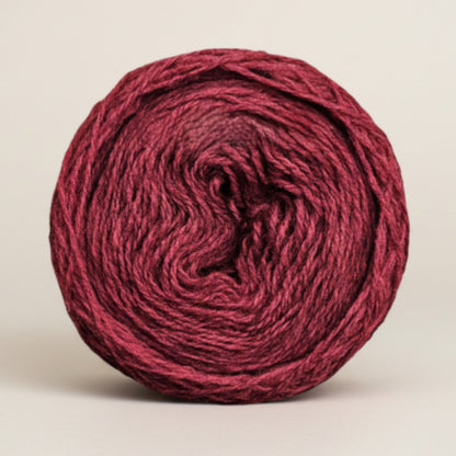 A round cake of Uradale 100% Shetland wool yarn in a deep burgundy Selfheal colourway.