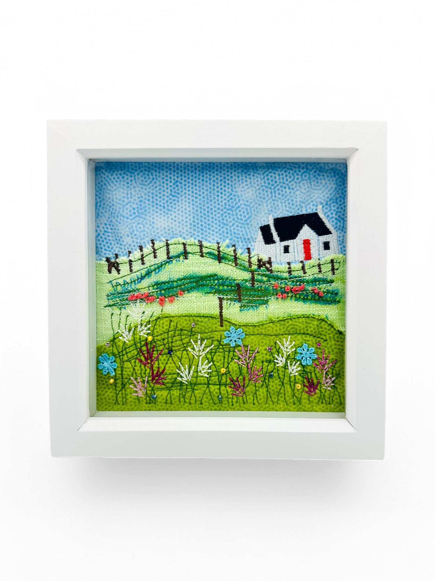 Framed artwork of a croft house and landscape with flowers on a white background