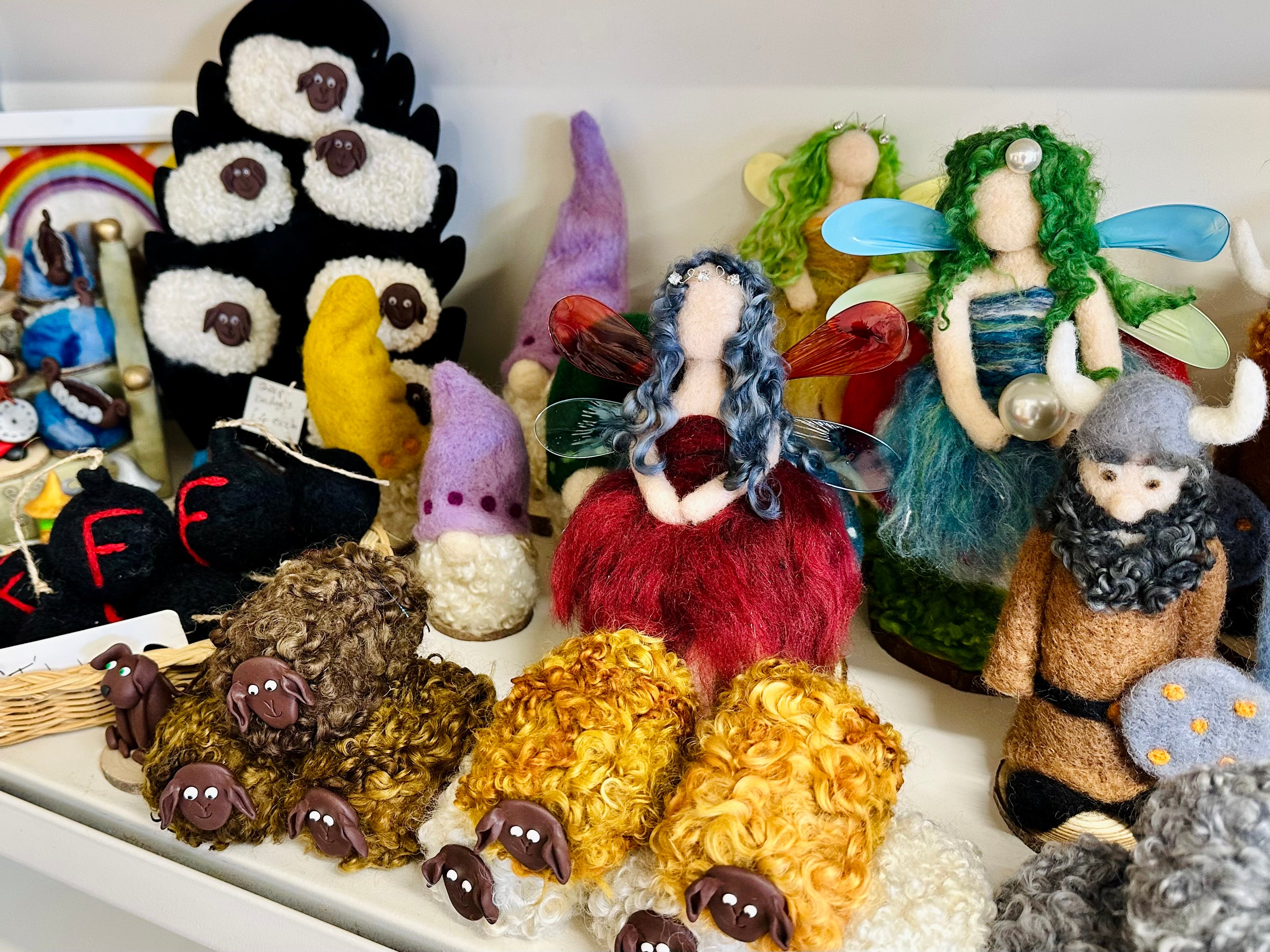 Collection of handmade felted dolls and creatures on a white surface.