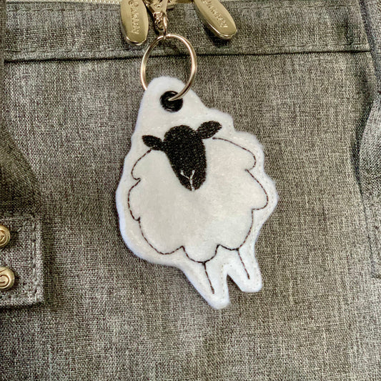 Shetland sheep keyring made of white felt with black face and brown stitching.