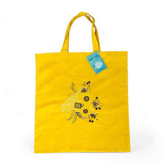 Yellow tote bag with an embroidered bee and flowers.