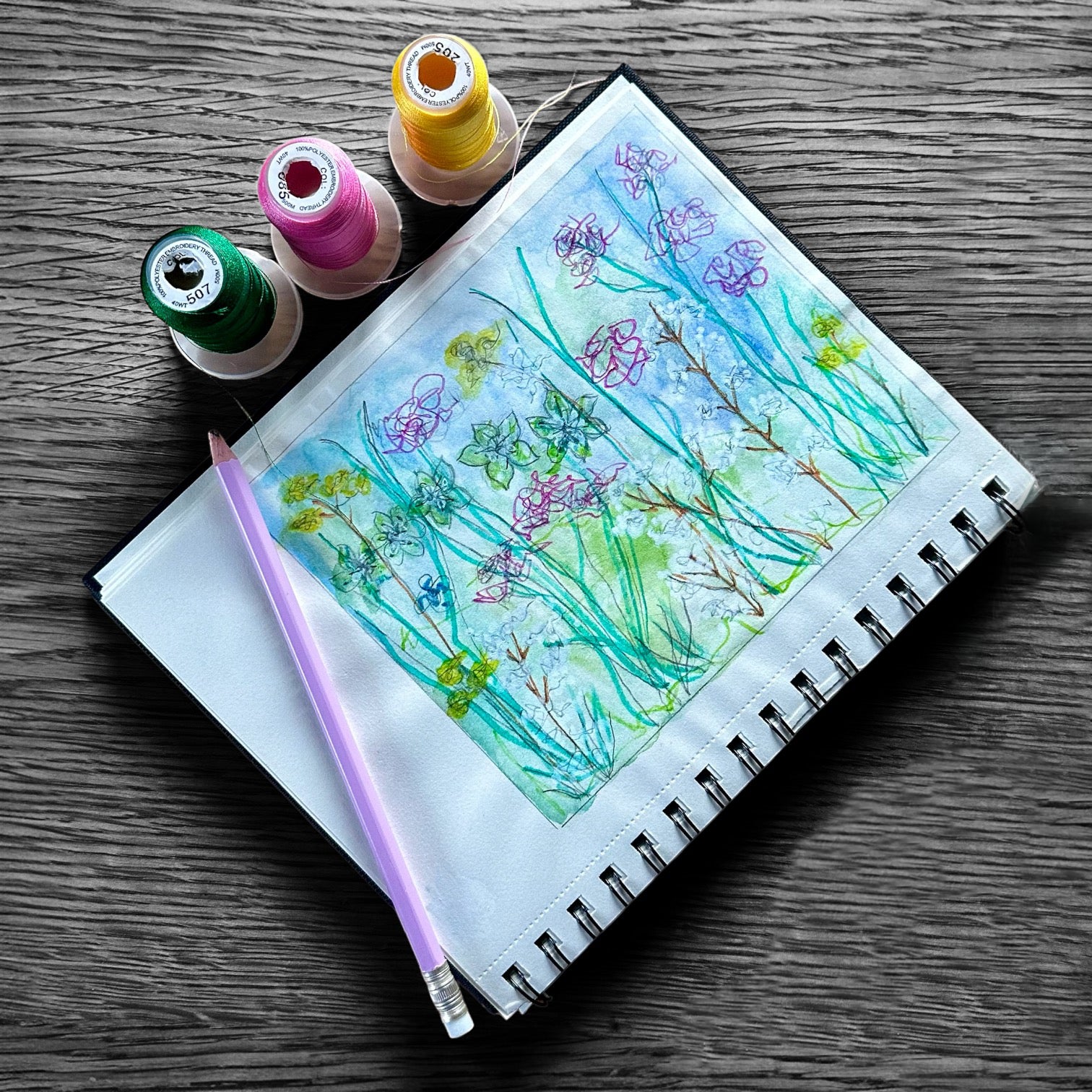 Artistic drawing of plants on a notebook with spools of thread in the background