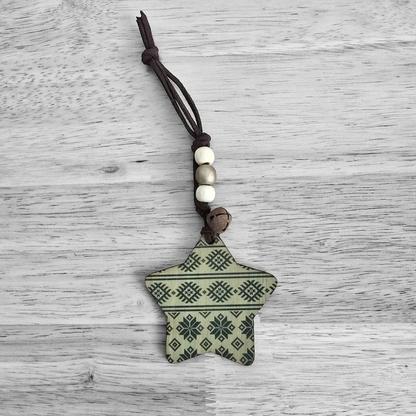 A wooden star ornament with a patterned design hangs from a cord with beads and a bell.